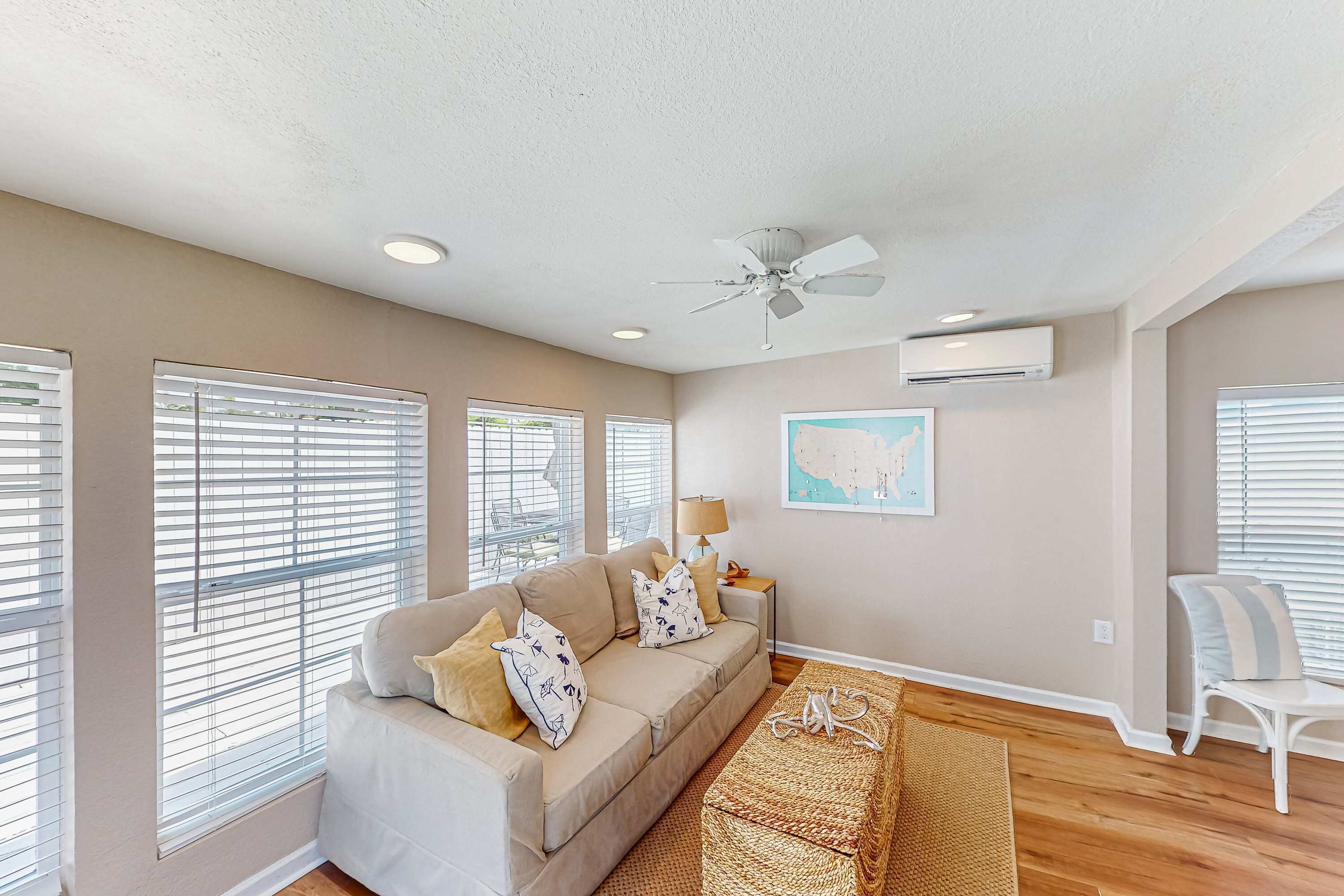 A spacious living room with a beige sofa, a woven rug, and a ceiling fan.