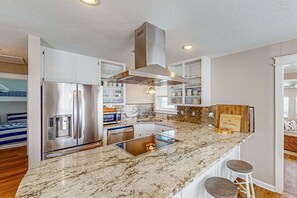 A modern kitchen with a stainless steel refrigerator, a built-in oven, and a large island with stools. - Bright home near the beach with enclosed patio, grill, outdoor shower, W/D, AC (Santa Rosa Beach)