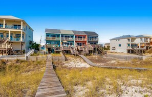 A beachfront property with a wooden boardwalk leading to colorful multi-story buildings with balconies. - Beachfront Townhome with Beautiful Gulf Views, Decks, WiFi, Laundry, & AC! (Navarre Beach)