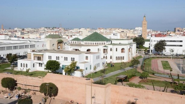 Un grand bâtiment blanc surmonté d’un dôme vert et d’un haut minaret, entouré de bâtiments plus petits et se dressant sous un ciel dégagé.