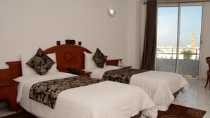Une chambre d’hôtel avec deux lits, une tête de lit en bois, une table de chevet, une petite table et une vue sur le paysage urbain par une grande fenêtre.