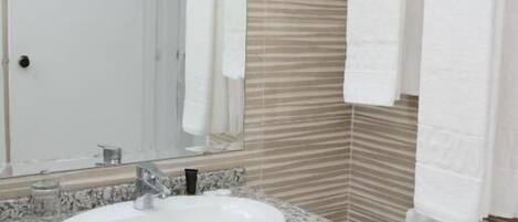 A bathroom with a granite countertop sink, a mirror, and striped beige tiles.
