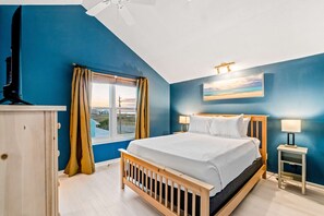 A bedroom with a large bed, a window with curtains, a nightstand with a lamp, and a ceiling fan. - Lovely home with sound view, balcony, full kitchen, central AC, & washer - dryer (Navarre Beach)
