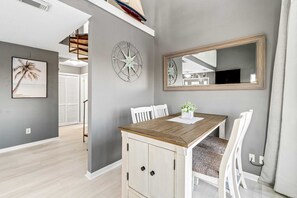 A dining area with a wooden table, white chairs, a wall-mounted compass, and a large mirror. - Lovely home with sound view, balcony, full kitchen, central AC, & washer - dryer (Navarre Beach)
