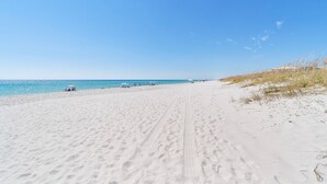 Une plage de sable où l’on peut voir des empreintes de pas menant à l’eau, un ciel dégagé et une vue lointaine sur la mer.