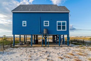 A two-story blue house with a covered porch, a water tank, and a small table and bench. - Lovely home with sound view, balcony, full kitchen, central AC, & washer - dryer (Navarre Beach)
