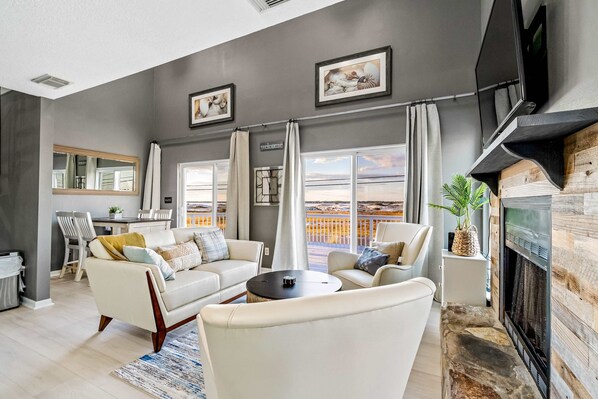 A modern living room with a fireplace, large windows, and a view of the ocean. - Lovely home with sound view, balcony, full kitchen, central AC, & washer - dryer (Navarre Beach)