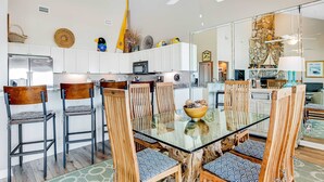 A modern kitchen with white cabinets, a central island, and a dining area with wooden chairs and a glass table. - Gorgeous condo with ocean views, inviting balcony, bright interior, washer/dryer (Santa Rosa Beach)