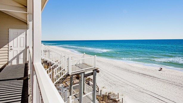 A beach view from a building with a wooden deck and a white door. - Gorgeous condo with ocean views, inviting balcony, bright interior, washer/dryer (Santa Rosa Beach)