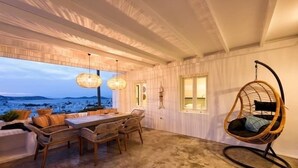 A cozy dining area with a table and chairs, a hanging chair, and a view of the mountains. - Naousa Story 1 ❤ (Paros)