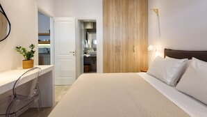 A modern bedroom with a large bed, a bedside table, a clear chair, a wooden wardrobe, and a bathroom visible through an open door. - Naousa Story 1 ❤ (Paros)