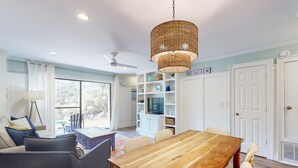 A dining area with a wooden table and chairs, a wicker pendant light, and a view of the outdoors through large windows. - Bright Townhouse with High-Speed WiFi, Private Washer&Dryer, and Pool (Santa Rosa Beach)