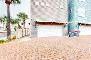 Un quartier résidentiel avec une porte de garage, une clôture blanche en bois et deux poubelles portant l’inscription « MATE’S ».