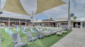 An outdoor seating area with Adirondack chairs and a green turf, a building with 'CRAVE BURGERS' signage, and a 'LIVE SHOP' sign. - Completely Remodeled Beachside Studio with Pool - Snowbirds Welcome (Inlet Beach)