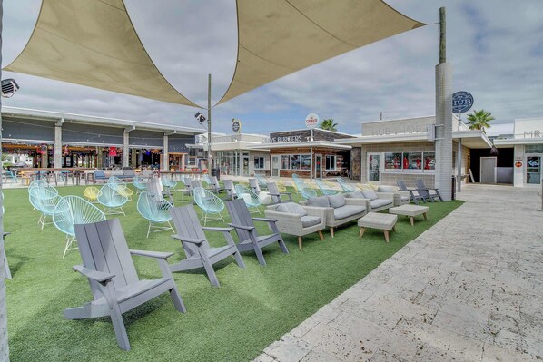 An outdoor seating area with Adirondack chairs and a green turf, a building with 'CRAVE BURGERS' signage, and a 'LIVE SHOP' sign. - Completely Remodeled Beachside Studio with Pool - Snowbirds Welcome (Inlet Beach)