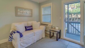 A living room with a white couch, a small table, and a large window with blinds. - Completely Remodeled Beachside Studio with Pool - Snowbirds Welcome (Inlet Beach)