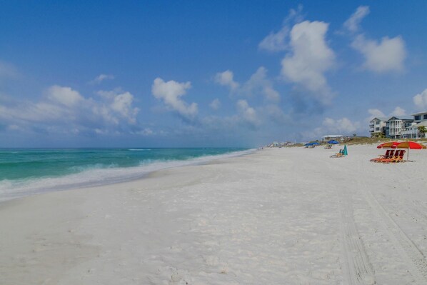 Ein Strand mit weißem Sand, blauem Himmel und einigen Gebäuden im Hintergrund.