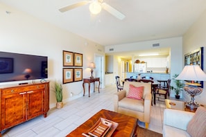 A living room with a flat-screen TV, wooden cabinet, and a ceiling fan. - Spacious, waterfront condo with furnished balcony, pools & fitness room (Panama City Beach)