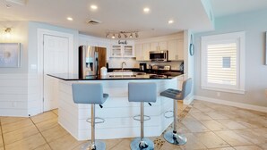 Una cocina moderna con una isla central, taburetes de bar y vistas al exterior.