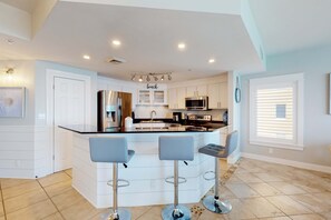 A modern kitchen with a central island, bar stools, and a view of the outside. - Open & spacious condo in beachfront complex with pool, gym, elevator & fast WiFi (Panama City Beach)