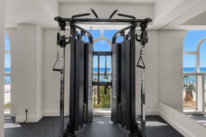 A gym with a pull-up bar and weight machines, large windows with a view of the beach. - Open & spacious condo in beachfront complex with pool, gym, elevator & fast WiFi (Panama City Beach)