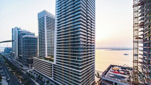 Um edifício alto com várias varandas, vista para a água e uma grua de construção nas proximidades.