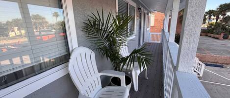 A covered porch with white chairs and a potted plant, a number '1691' on the wall, and a view of the parking lot.