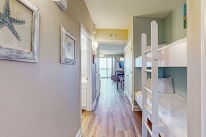 A narrow hallway with wooden flooring, bunk beds on the right, and framed artwork on the walls. - Beachy oceanfront condo w/ beach access, shared pools and hot tub, & free WiFi (Panama City Beach)