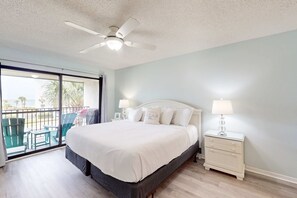 Une chambre avec un lit, une table de chevet, un ventilateur de plafond et une vue sur le balcon extérieur.