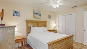 A bedroom with a wooden bed, a nightstand, a lamp, and a ceiling fan. - Beachy townhouse with 11 pools, golf, fast WiFi & private WD (Panama City Beach)