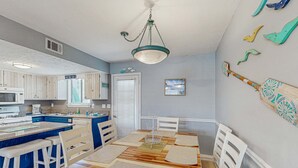 A kitchen with wooden cabinets, a central island, and a dining area with a wooden table and white chairs. - Beachy townhouse with 11 pools, golf, fast WiFi & private WD (Panama City Beach)