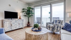Ein Wohnzimmer mit einem großen Flachbildfernseher, einem Holztisch, einem gemusterten Sessel und einer Topfpflanze.