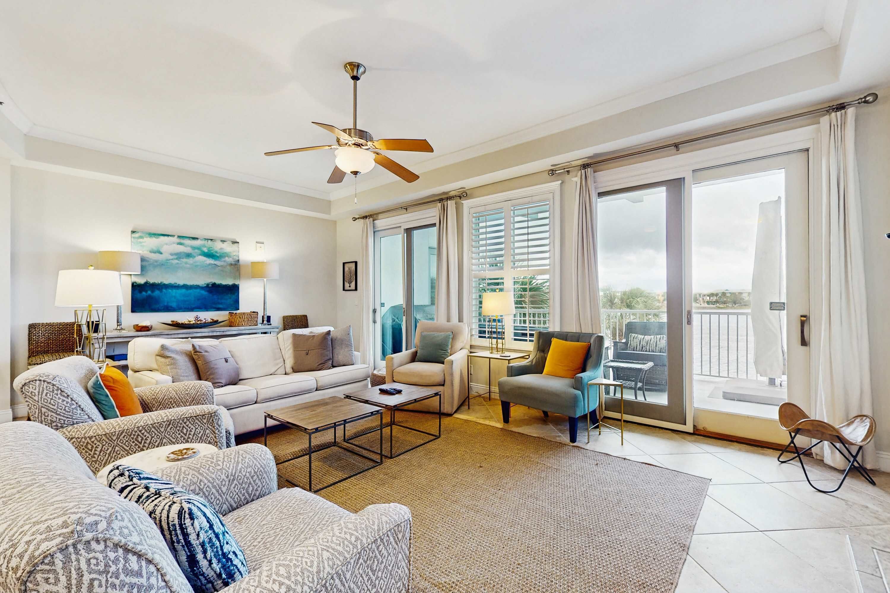 A spacious living room with a sofa set, a coffee table, and a TV. There is a balcony with a chair and a table.