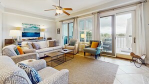 Ein geräumiges Wohnzimmer mit einer Sofagarnitur, einem Couchtisch und einem Fernseher. Es gibt einen Balkon mit einem Stuhl und einem Tisch.