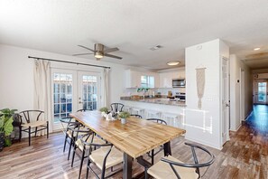Cocina moderna con armarios blancos, una isla central y un comedor con mesa y sillas de madera.
