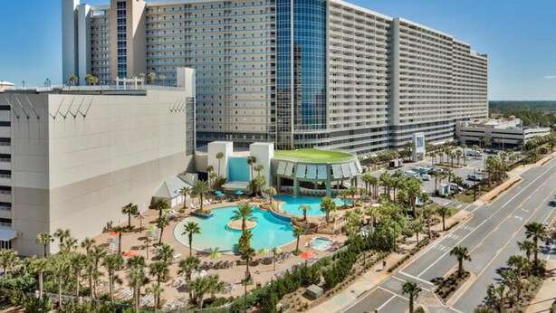 A large hotel with multiple floors, a swimming pool, and a parking area.