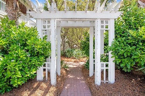 A white arbor with a brick pathway leading through it, surrounded by green foliage. - Beautiful, dog-friendly home with shared pools & complimentary beach chairs (Panama City Beach)