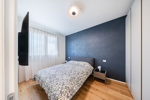 A bedroom with a bed, a nightstand, a wall-mounted TV, and a ceiling light.