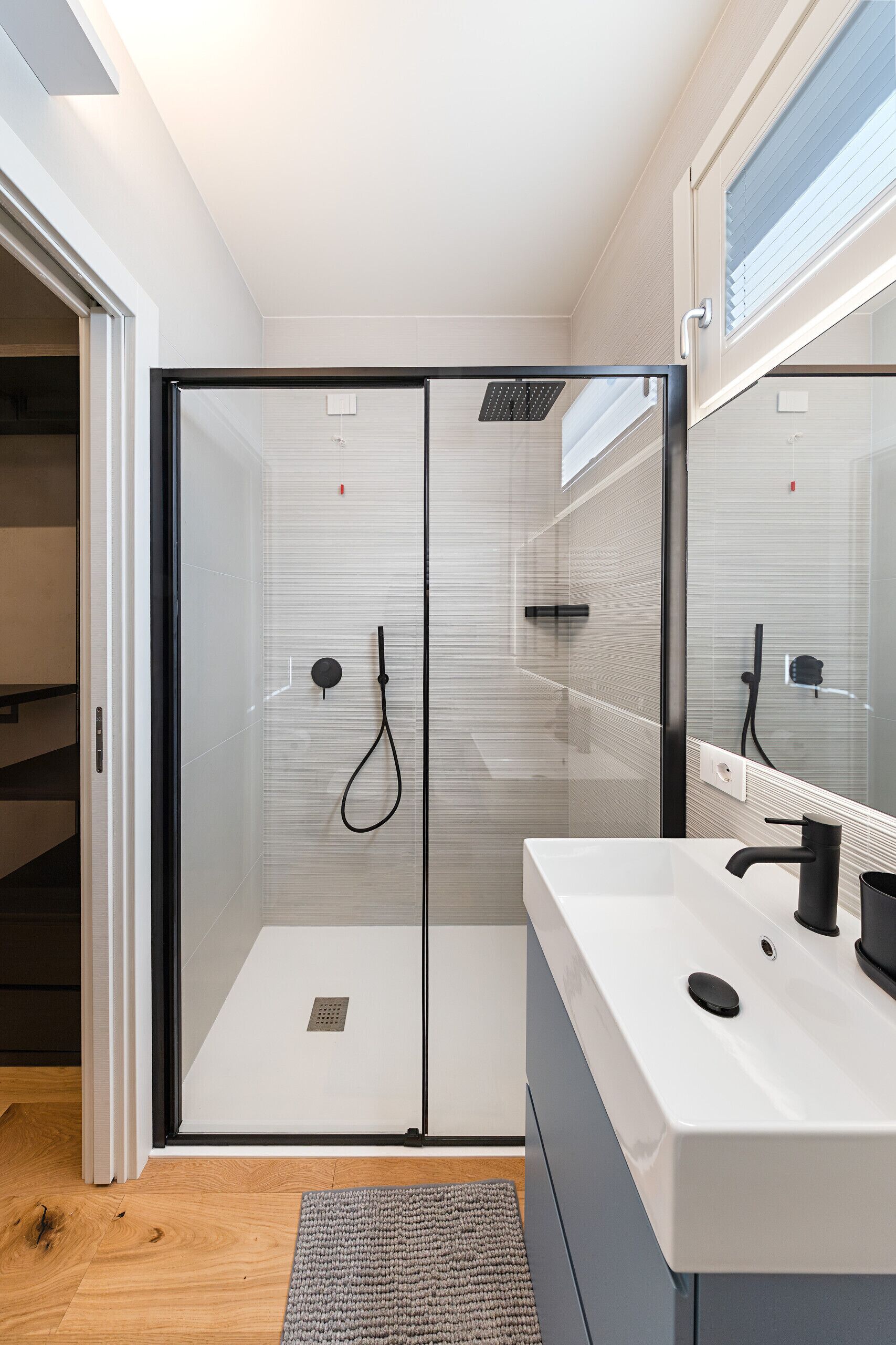 Ein modernes Badezimmer mit Duschkabine aus Glas, einem weißen Waschbecken und einem Spiegel.
