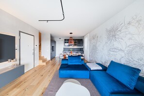 A modern living room with a blue sofa, a flat-screen TV, and a kitchen in the background.