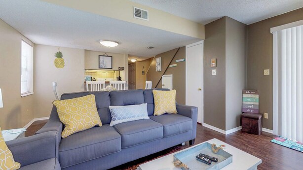 A living room with a gray sofa, patterned cushions, a coffee table with a remote control, and a sign with directional arrows. - Bright condo in gated community with pool, hot tub & tennis (Panama City Beach)