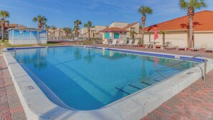 A swimming pool with clear blue water, surrounded by palm trees and lounge chairs. - Bright condo in gated community with pool, hot tub & tennis (Panama City Beach)