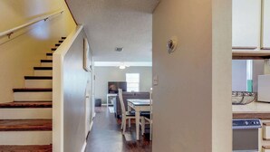A hallway with wooden stairs leading to a dining area with white chairs and a table. - Bright condo in gated community with pool, hot tub & tennis (Panama City Beach)