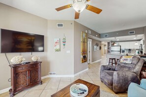 A living room with a flat-screen TV, a wooden cabinet, a recliner, and a coffee table. - Beachfront Condo, gorgeous views, dog-friendly, shared pool and beach access (Panama City Beach)