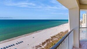 Blick auf einen Strand vom Balkon aus, mit blauem Himmel, Sandstrand und einem Pier in der Ferne.