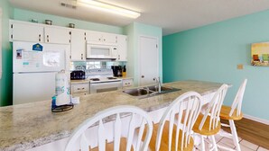 A kitchen with white cabinets, a microwave, a sink, and a granite countertop. - Beachfront condo with true beachfront walkout, patio, BBQ area, & Gulf view (Panama City Beach)