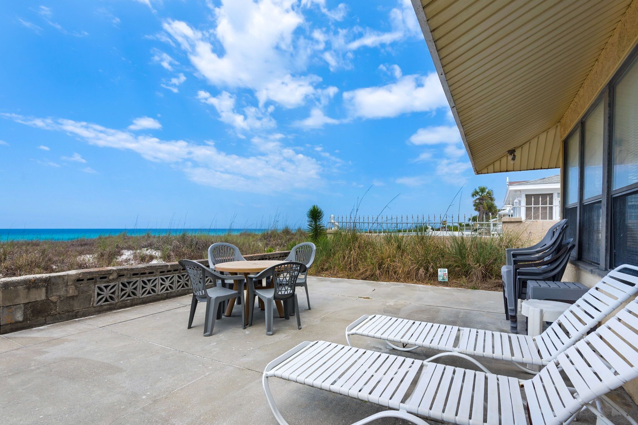 A patio with a table and chairs, lounge chairs, and a view of the ocean.