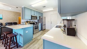 Una cocina moderna con armarios azules, una isla grande, electrodomésticos de acero inoxidable y taburetes de madera.