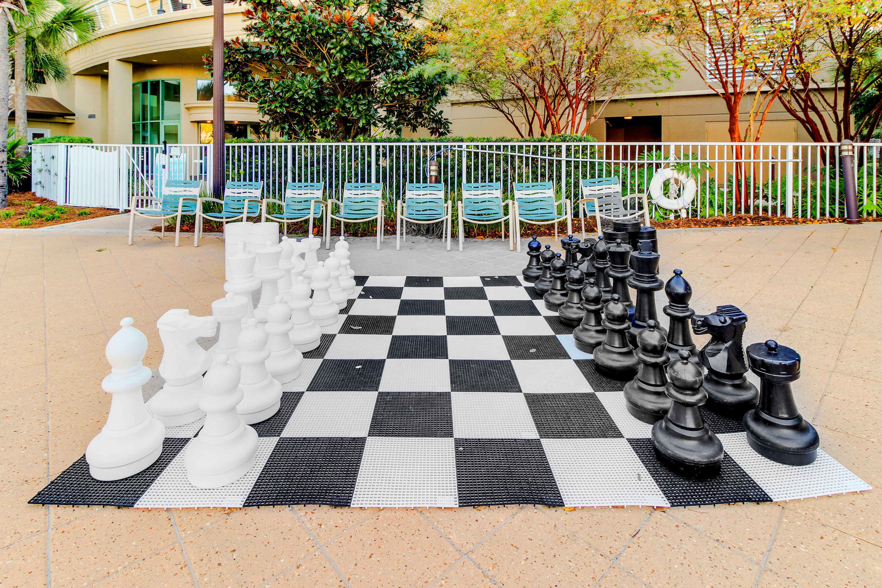 A large outdoor chessboard with oversized chess pieces set up in a courtyard.