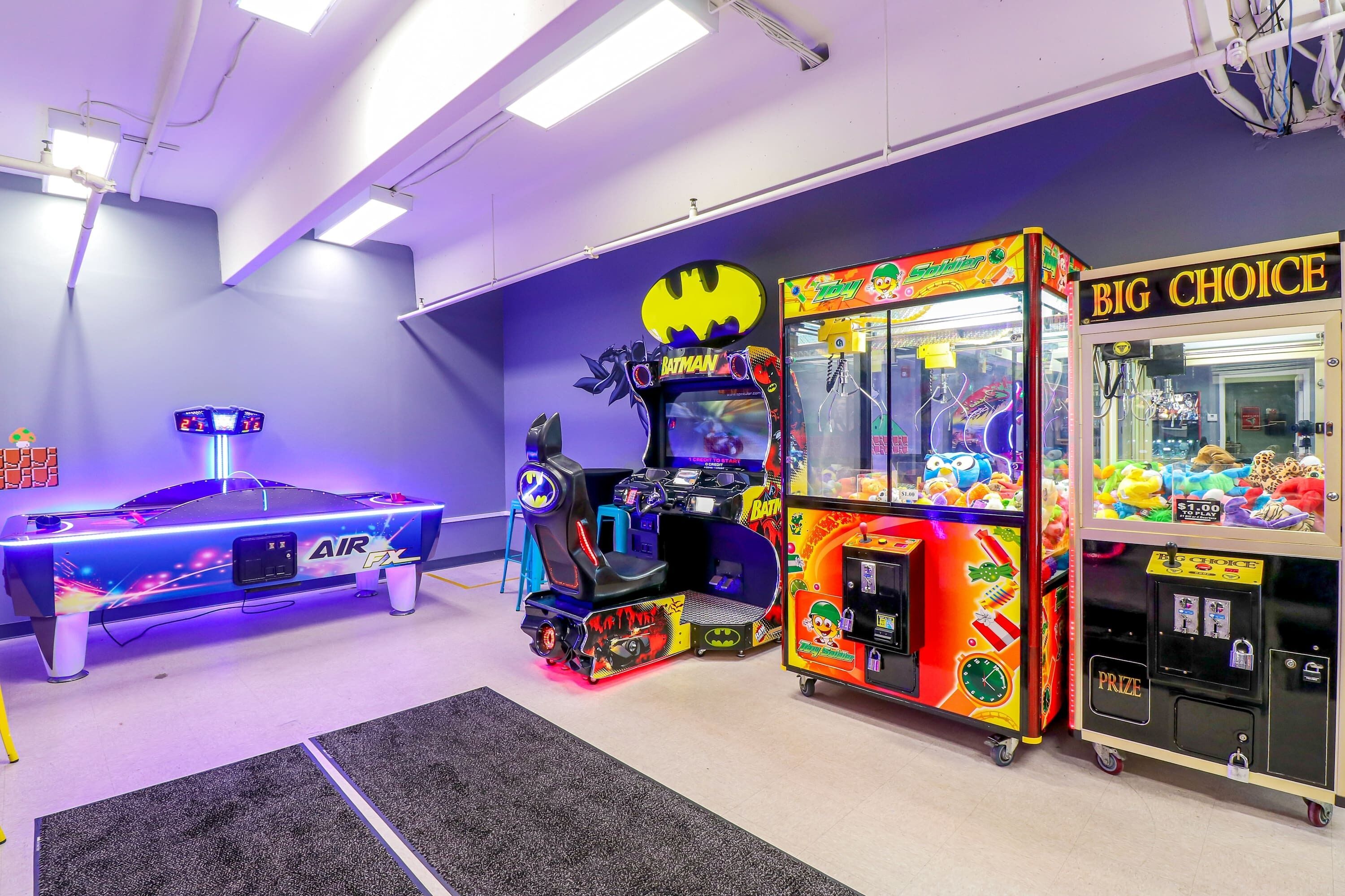 A room with a pool table, a Batman-themed arcade machine, and a claw machine.